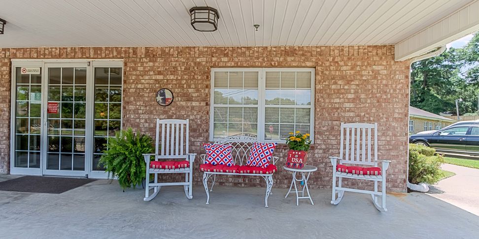 A cozy front porch with rocking chairs and decorative cushions against a brick wall.