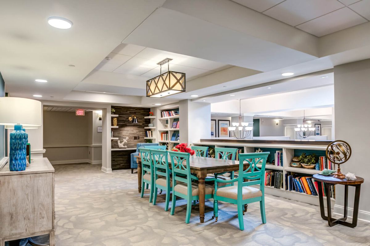 A modern dining area with turquoise chairs and a stylish chandelier, complemented by surrounding bookshelves.