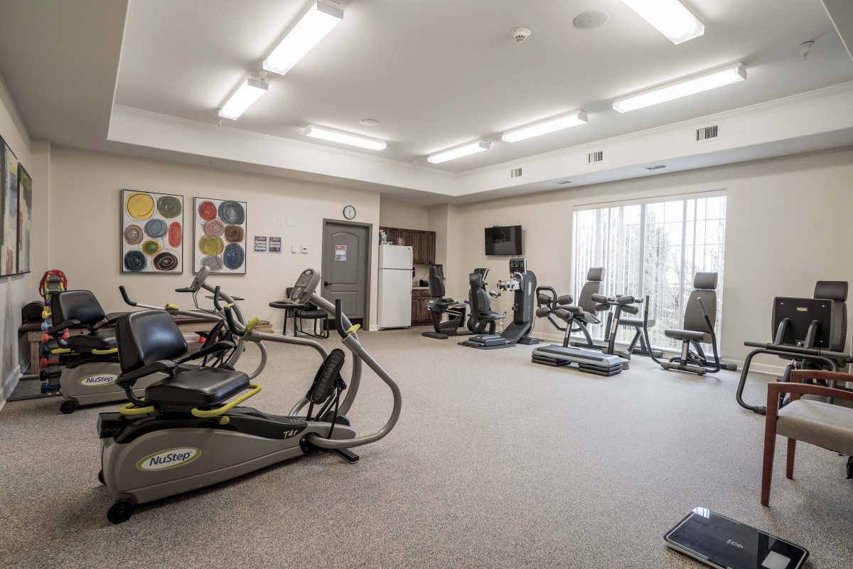 A well-equipped indoor gym with various exercise machines and ample lighting.