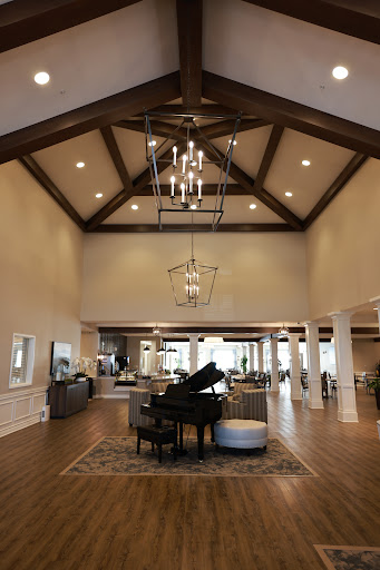 A spacious and elegantly designed living room featuring high ceilings, wooden beams, and a grand piano.