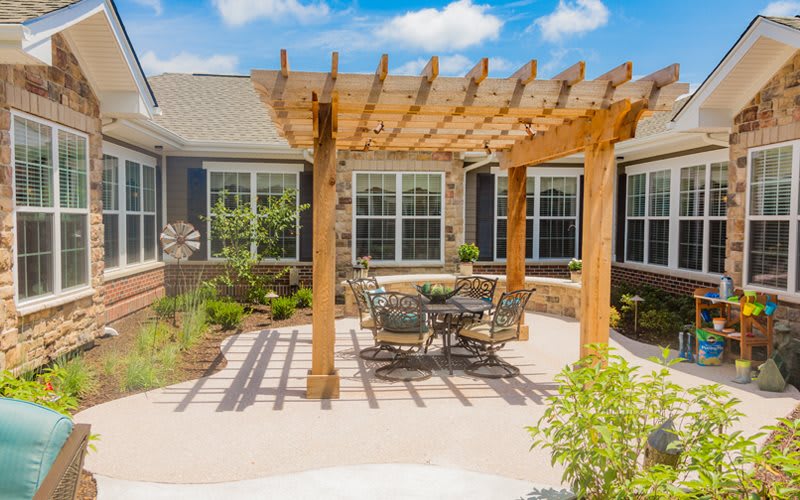 A sunny patio with a wooden pergola and outdoor seating, surrounded by a well-maintained garden.