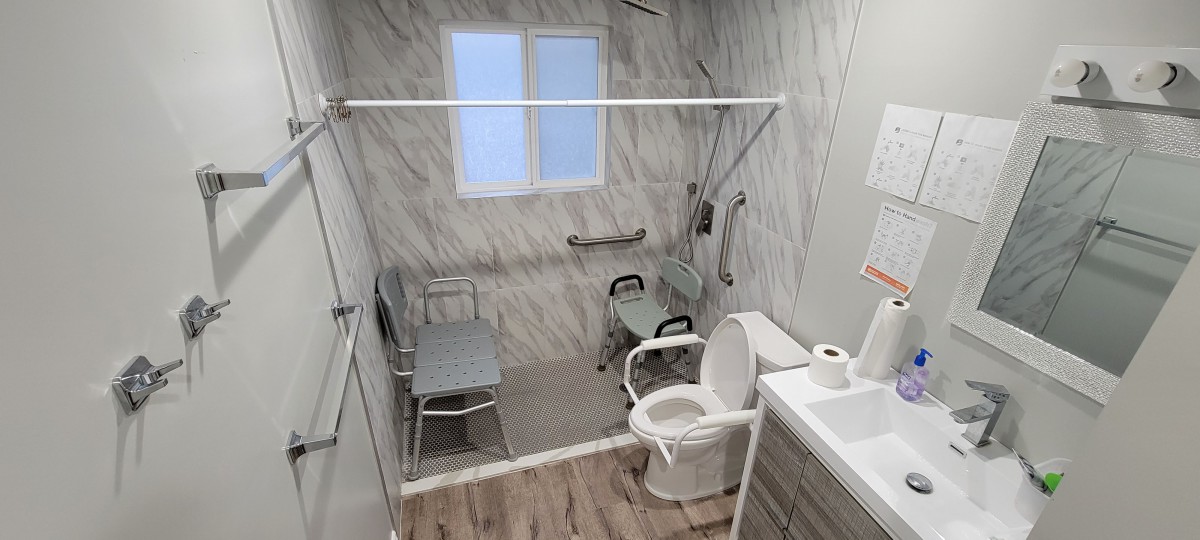 A modern, accessible bathroom featuring a walk-in shower with grab bars and a mobility aid chair.