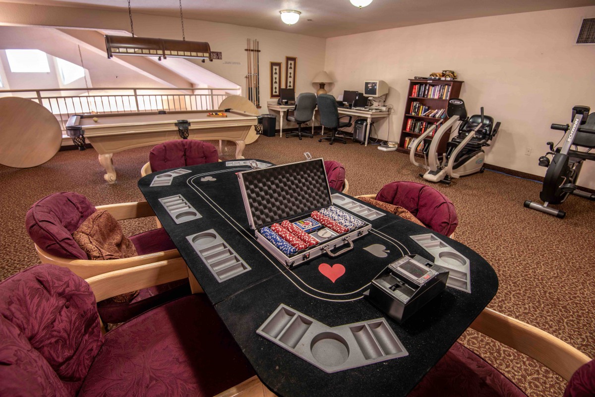 A cozy room with a poker table set up for a game night, featuring casino chips and surrounded by comfortable seating. Exercise equipment can be seen in the background.