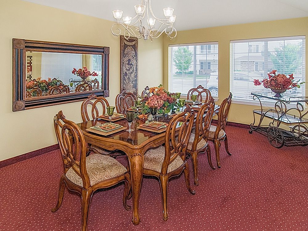 A well-furnished dining room with a large wooden table, surrounded by chairs, under a chandelier.
