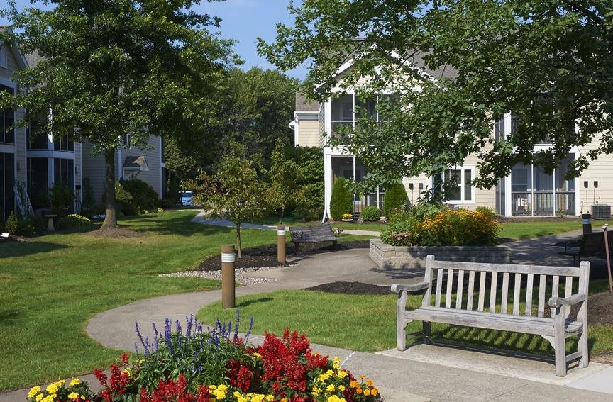 A peaceful garden scene with benches, flowers, and a house in the background.