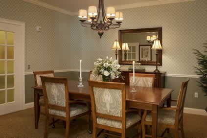 A cozy dining room with a wooden table, elegantly decorated with candles and flowers, under a classic chandelier.
