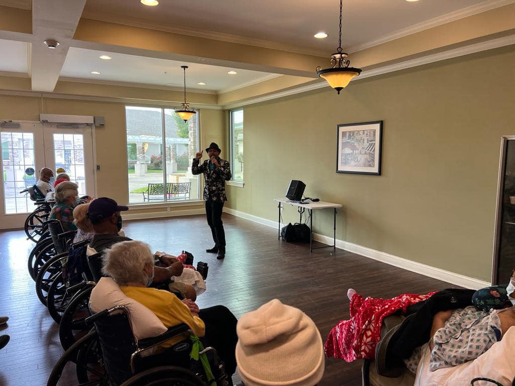 A speaker presents to an audience of elderly individuals in an indoor community setting.
