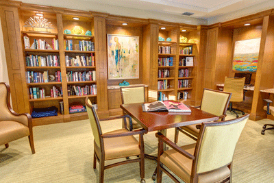 A cozy library room with wooden bookshelves, a central table, and chairs for reading.