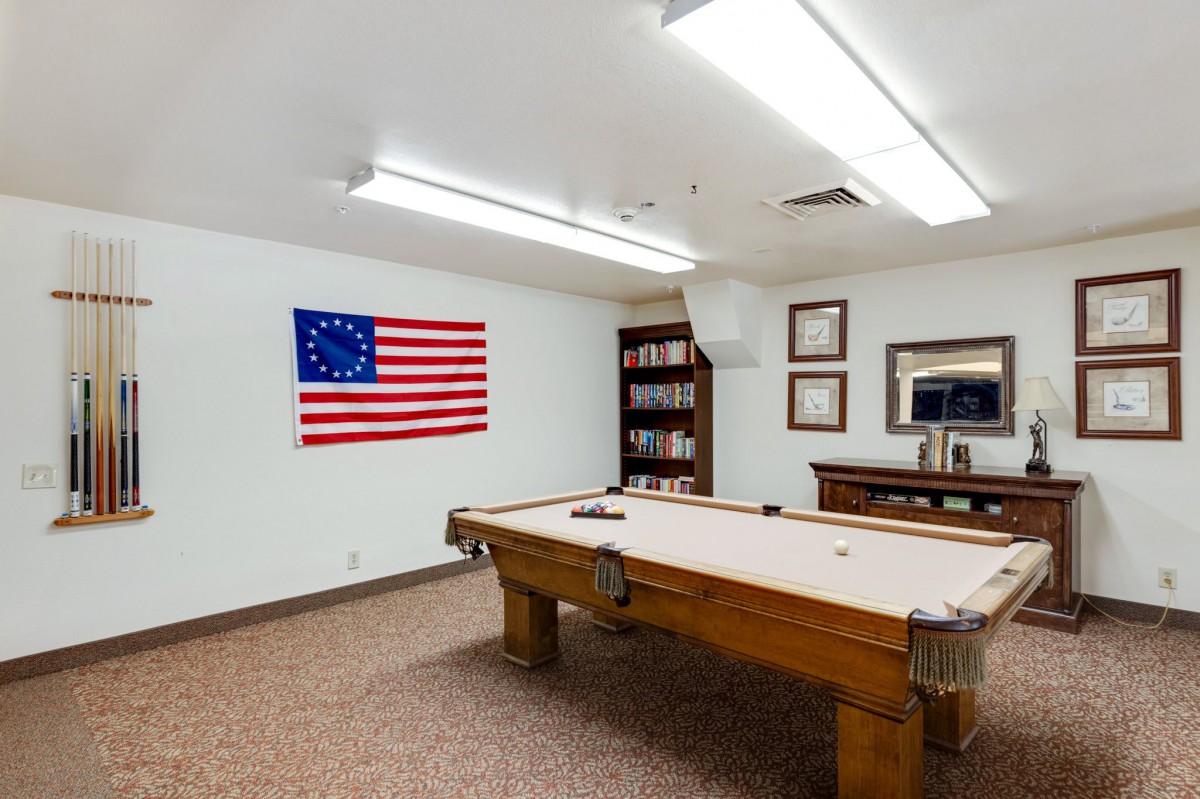 A cozy billiard room featuring a pool table, American flag, and shelves filled with books.