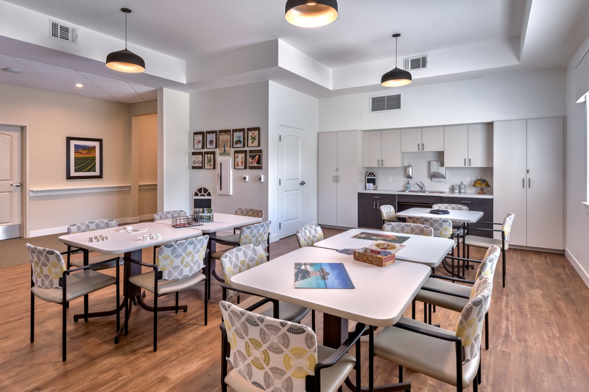 A modern conference room with tables and chairs, featuring a small kitchen area and stylish lighting.