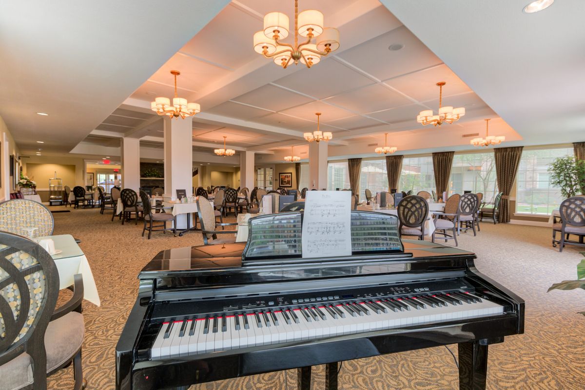 A grand piano in an elegantly furnished dining lounge with chandeliers and seating arrangements.