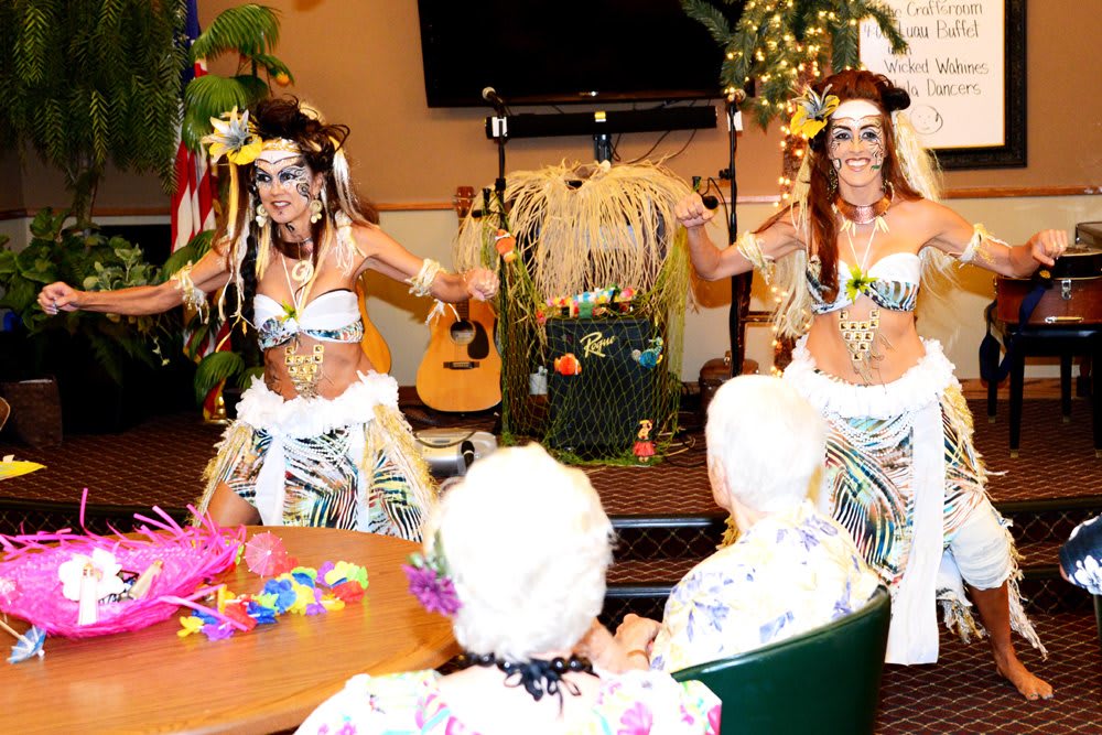 Hula dancers perform for an elderly audience in an indoor setting.