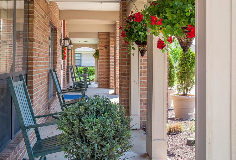 A cozy porch with rocking chairs and hanging plants, adorned with bright red flowers and surrounded by greenery.