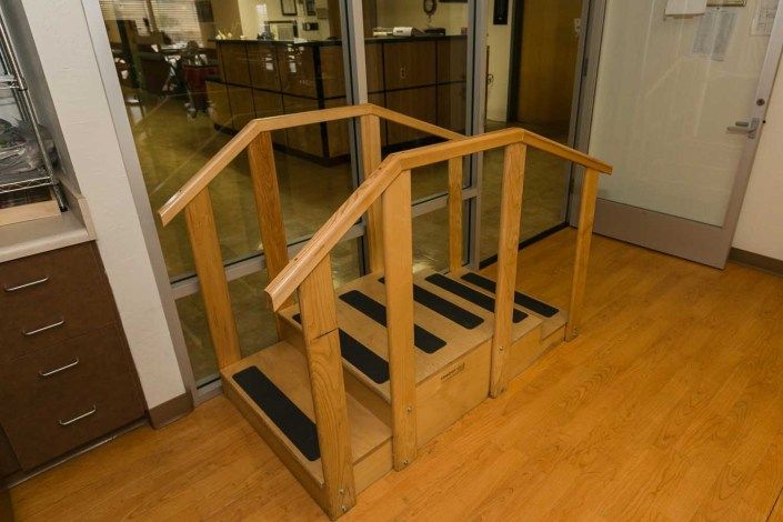 A set of small wooden stairs with handrails, commonly used in physical therapy and rehabilitation settings.