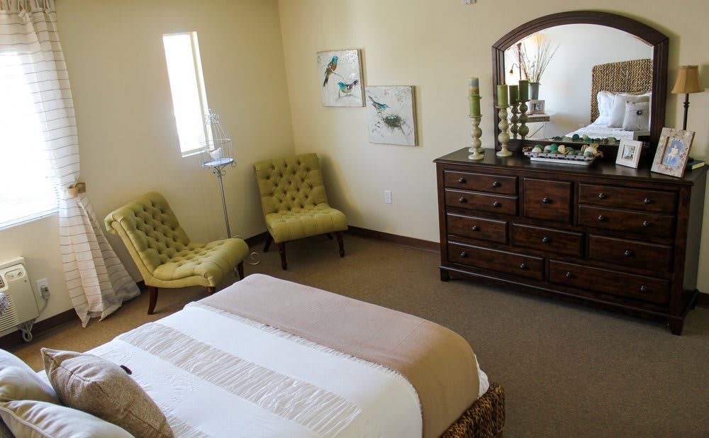 A cozy bedroom with elegant furniture, featuring a chest of drawers, two chairs, and wall art.