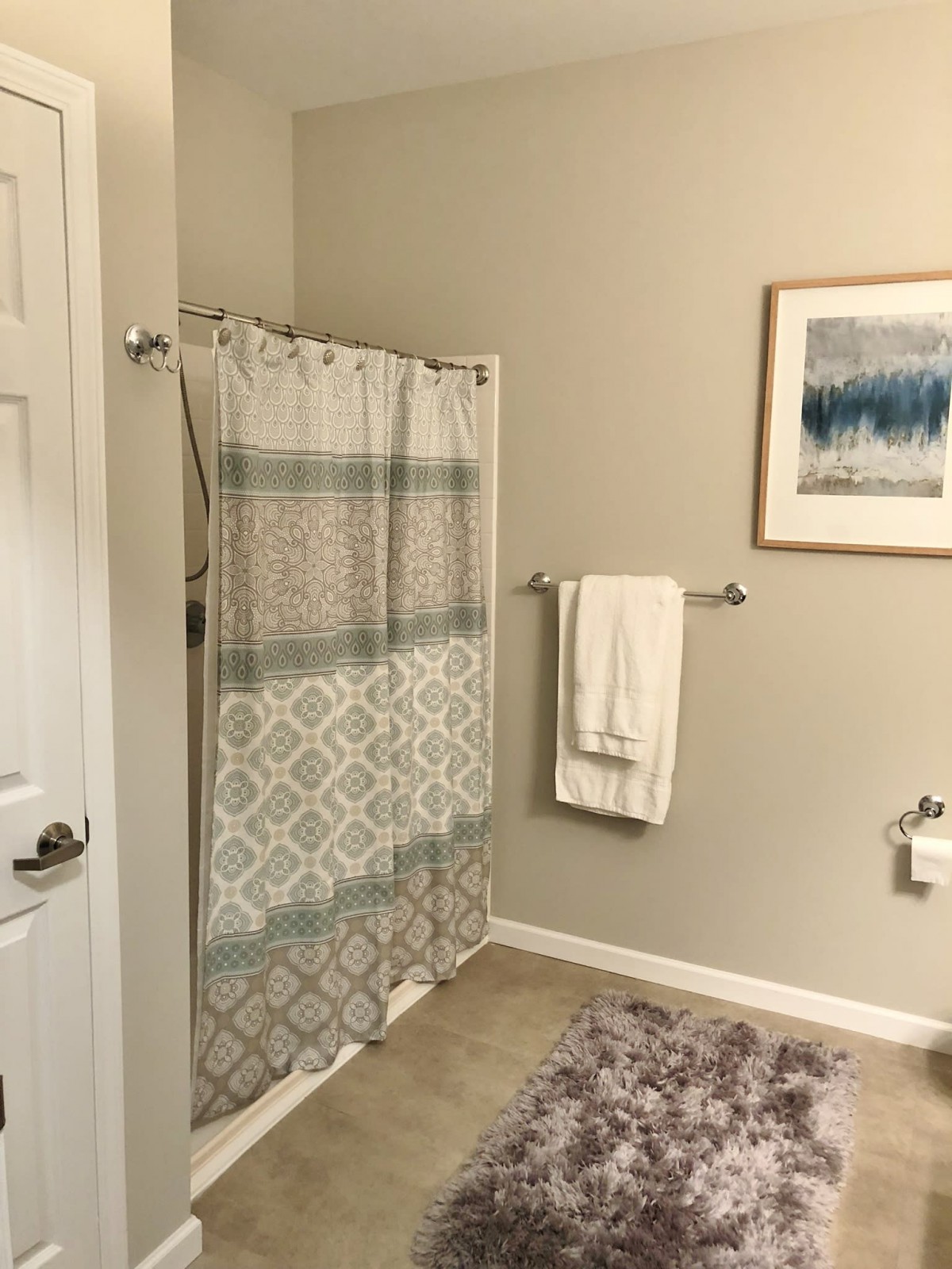 A tidy bathroom with a patterned shower curtain, a towel on a rack, and wall art.