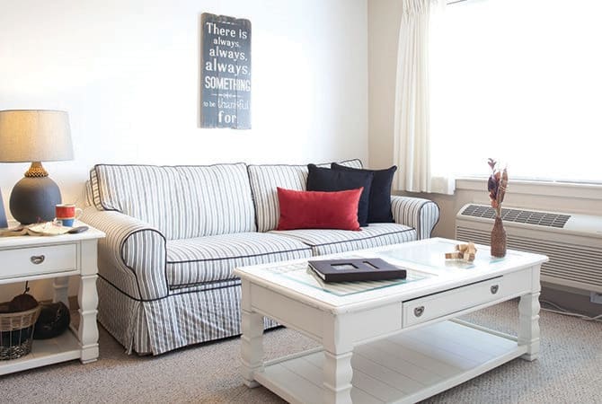 A modern living room with a striped sofa and colorful pillows, featuring a white coffee table and minimalist wall art.
