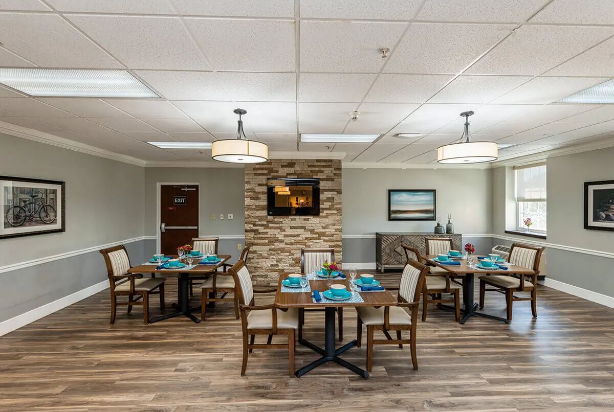 A cozy dining room featuring several tables and chairs, with a warm atmosphere enhanced by wood flooring and ambient lighting.