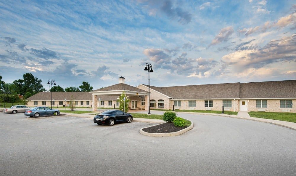A single-story building with a parking lot and a car parked in front, set against a cloudy sky backdrop.