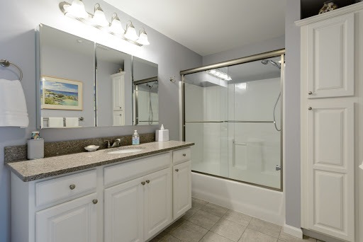 A modern and clean bathroom featuring a glass shower, white cabinetry, and ample lighting.