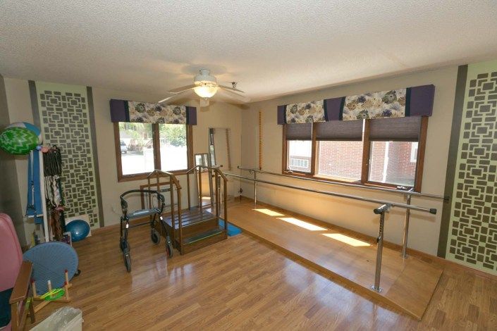 A well-lit rehabilitation room equipped with physical therapy apparatus, featuring parallel bars and exercise machines.