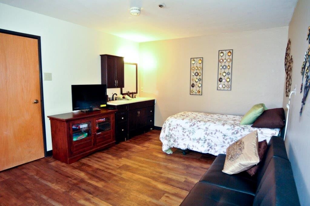 A cozy bedroom with a television, dresser, and a bed featuring floral bedding.