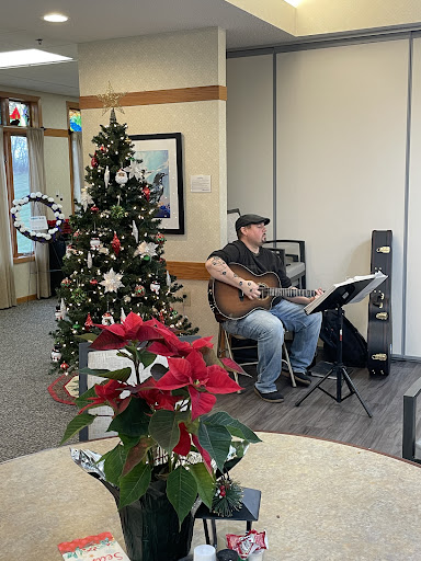 A musician performing with a guitar beside a beautifully decorated Christmas tree, adding a festive ambiance to the community space.