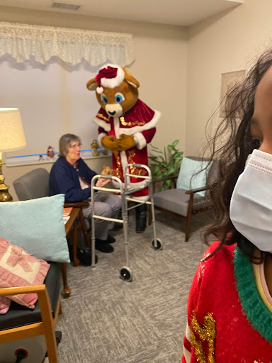 A festive visit to an assisted living facility during the holiday season, where a jovial bear mascot brings cheer.