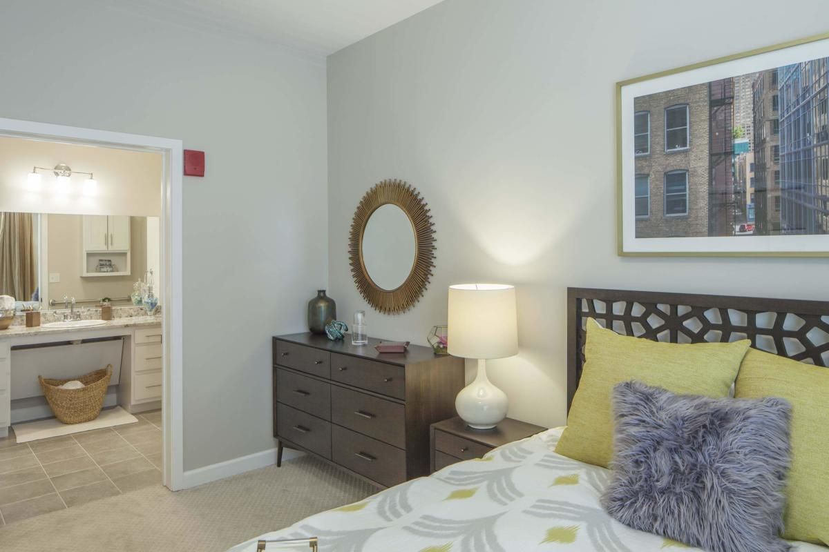 A cozy bedroom with a neatly arranged bed, a dresser with a mirror above it, and a lamp providing soft lighting.