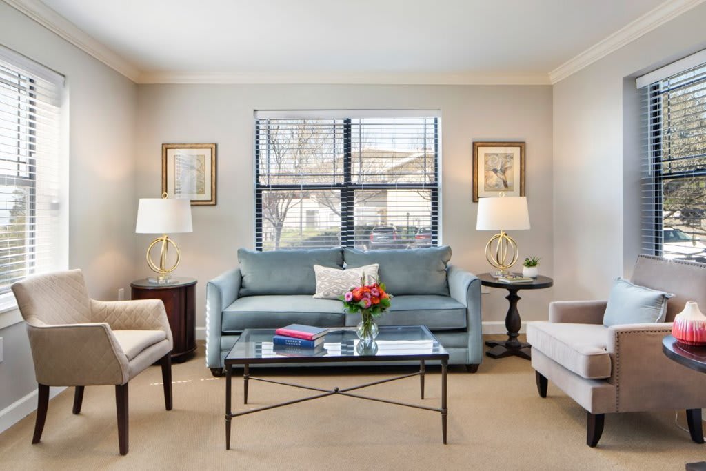 A cozy living room with a blue sofa, armchairs, and a glass coffee table adorned with flowers.