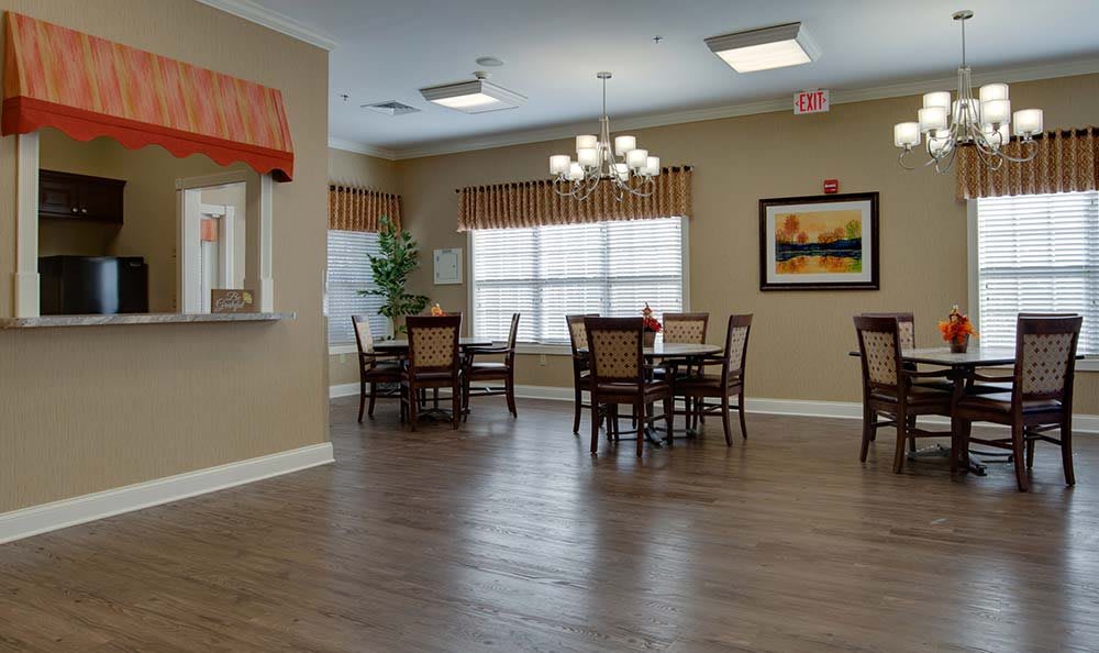 A well-lit dining area with multiple tables and chairs, featuring a chandelier and framed artwork on the wall.