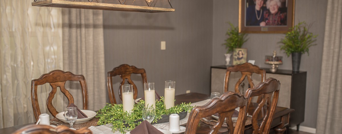 A cozy dining room setup featuring a wooden table adorned with candles and greenery under soft lighting.