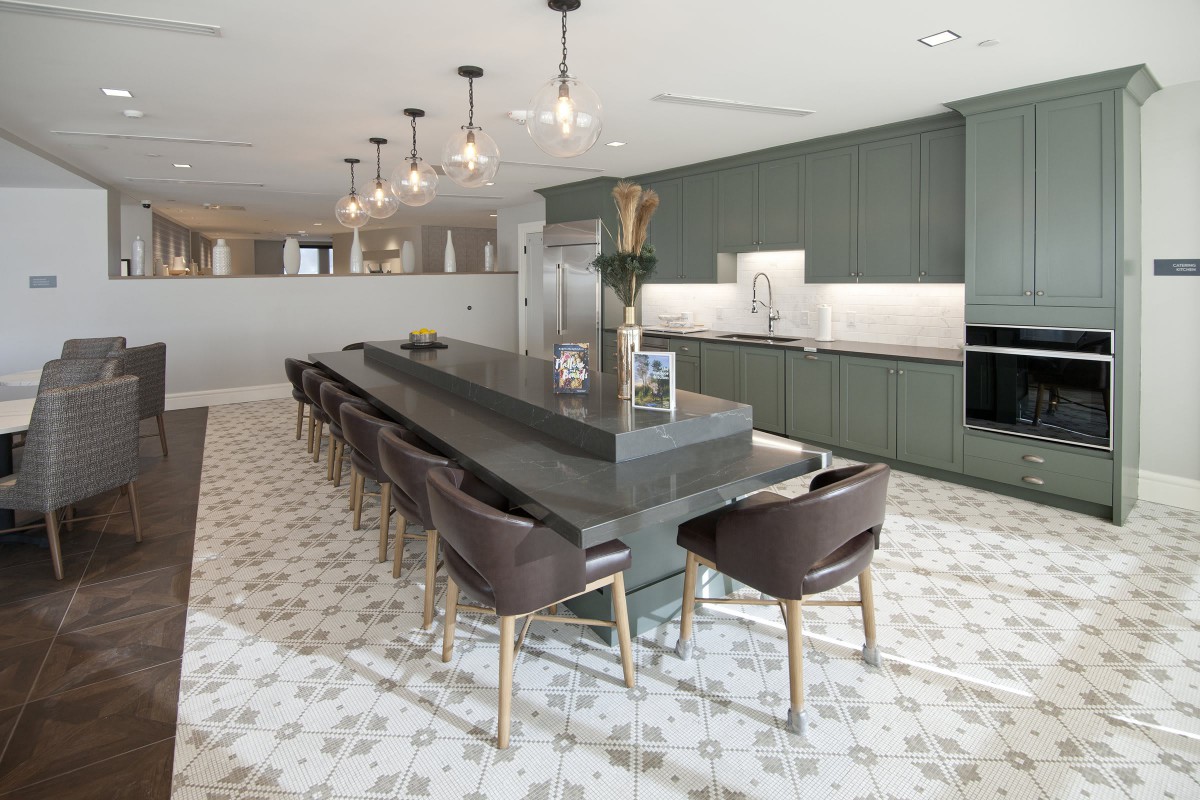 A modern kitchen with a large island and contemporary bar stools, featuring elegant lighting fixtures and a stylish marble floor.