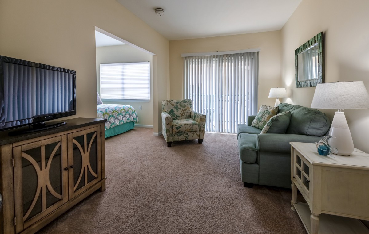 A cozy living room with a sofa and armchair, adjacent to a bedroom.