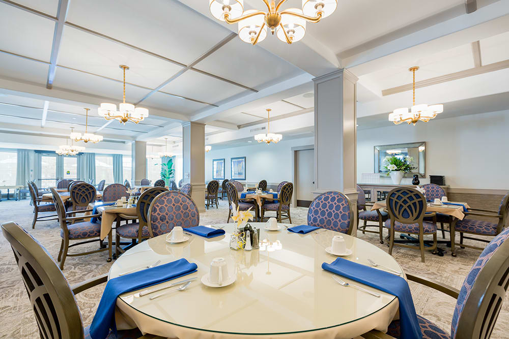 An elegant dining area with round tables, blue-accented chairs, and chandeliers.