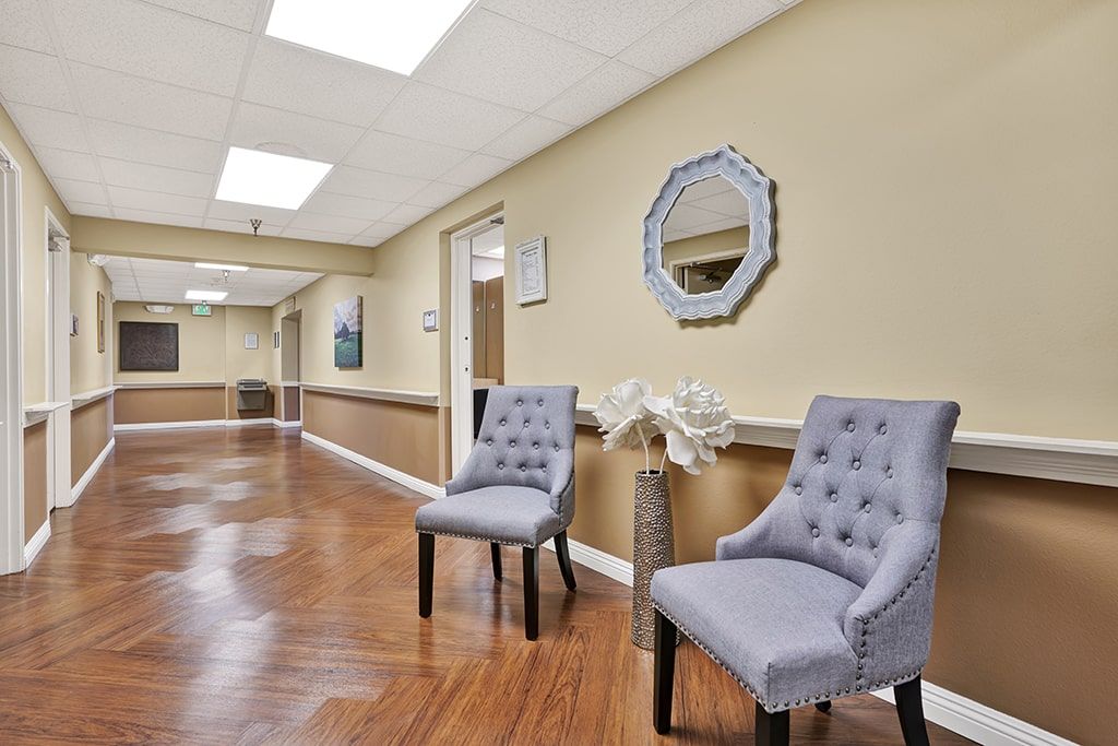 A hallway with upholstered chairs and decorative elements like a mirror and flowers.