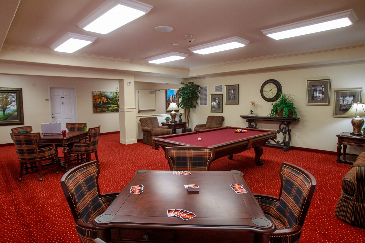 A cozy game room with a pool table and seating area on red carpet flooring.