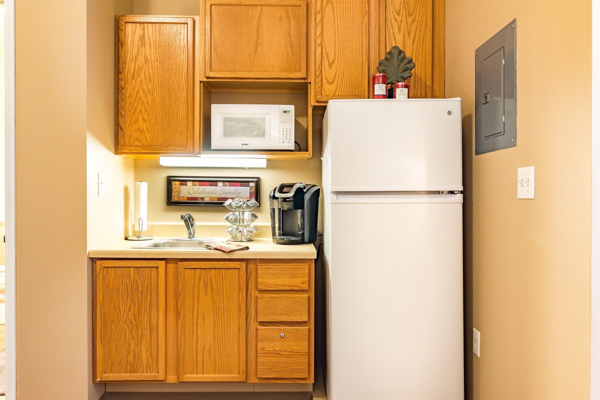 A compact kitchen setup with wooden cabinets, a white refrigerator, microwave, and a coffee maker.