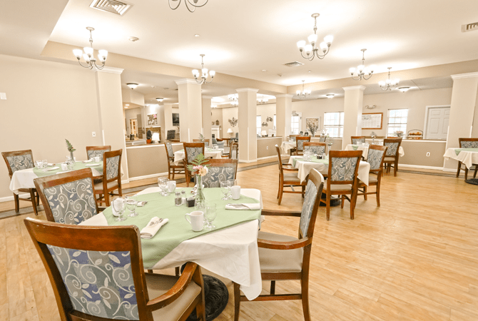 An elegant dining area with neatly arranged tables and chairs, featuring chandeliers and soft lighting.