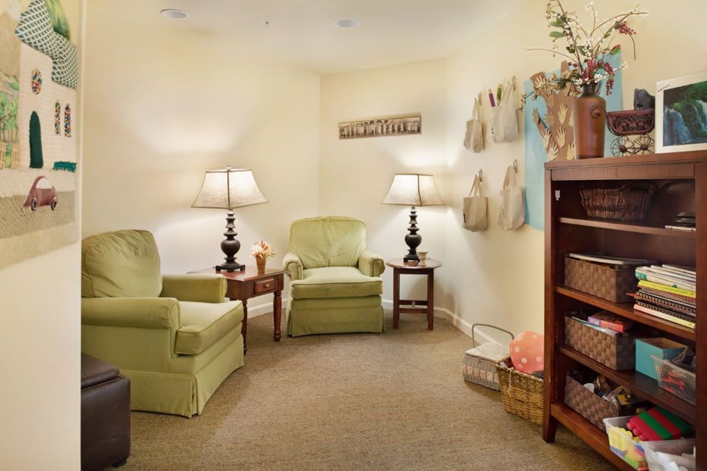 A cozy living room with green armchairs, warm lighting from table lamps, and decorative items on the walls and shelves.