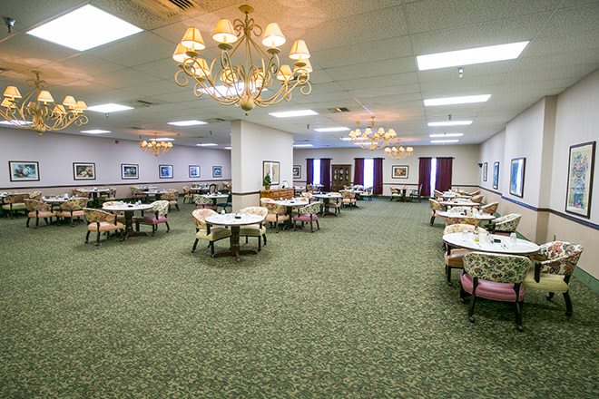 A spacious dining area with chandeliers, featuring several tables and chairs on a carpeted floor.