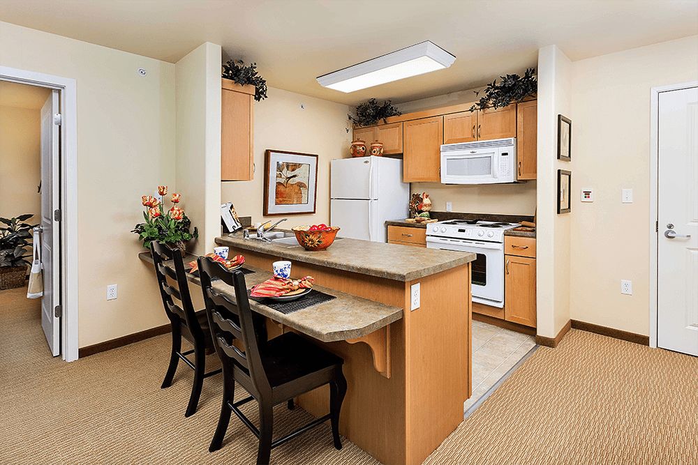 A cozy kitchen with a dining area featuring wooden cabinets, a countertop, bar stools, and modern appliances.