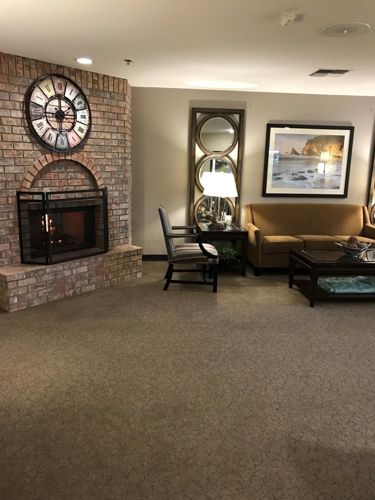 A cozy living room featuring a brick fireplace, large clock, and comfortable seating arrangement.