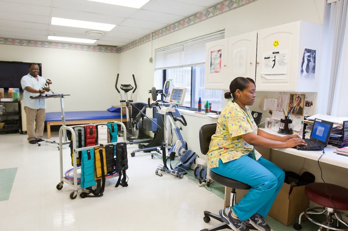 A nurse working at a desk in a medical office with exercise equipment.