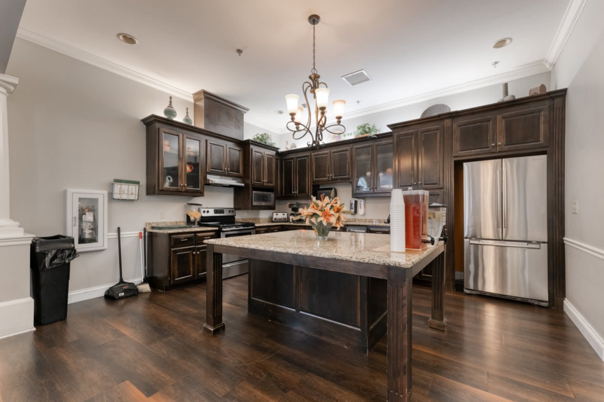 A modern kitchen featuring an island with dark wood cabinets, stainless steel appliances, and a chandelier.