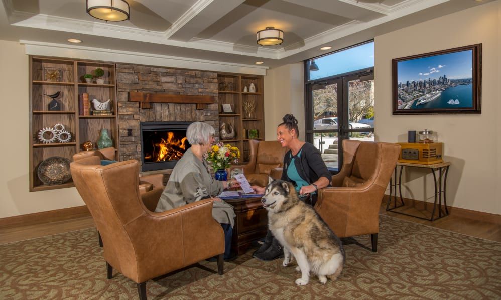 Two people having a conversation by the fireplace with a dog in a cozy living room.