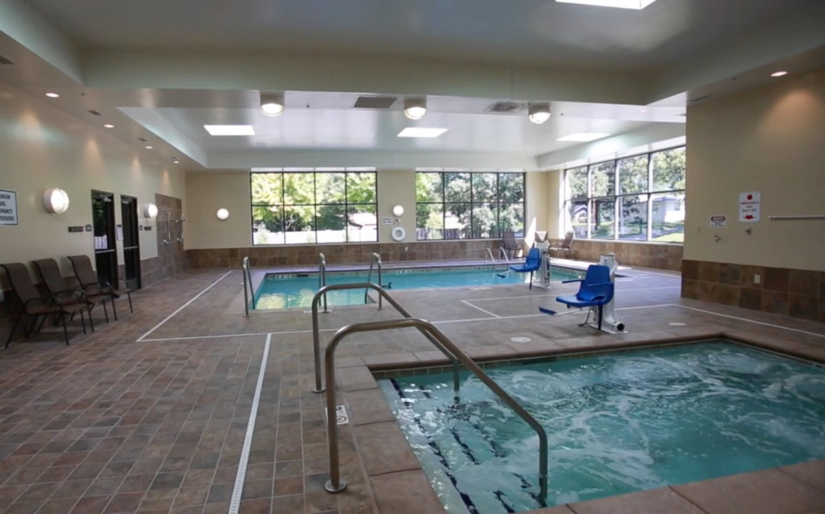 A spacious indoor swimming pool area featuring a hot tub and accessible lifts.
