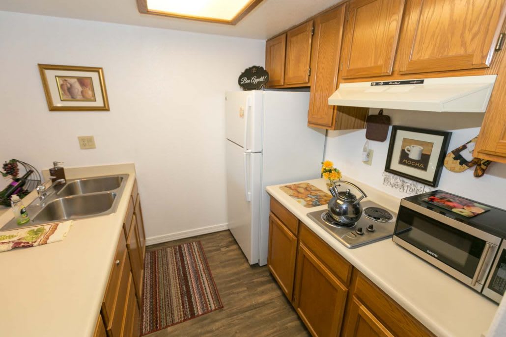 A compact kitchen with wooden cabinets, a refrigerator, sink, and microwave.