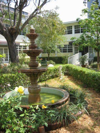 A serene garden with a decorative fountain and lush greenery in front of a building.