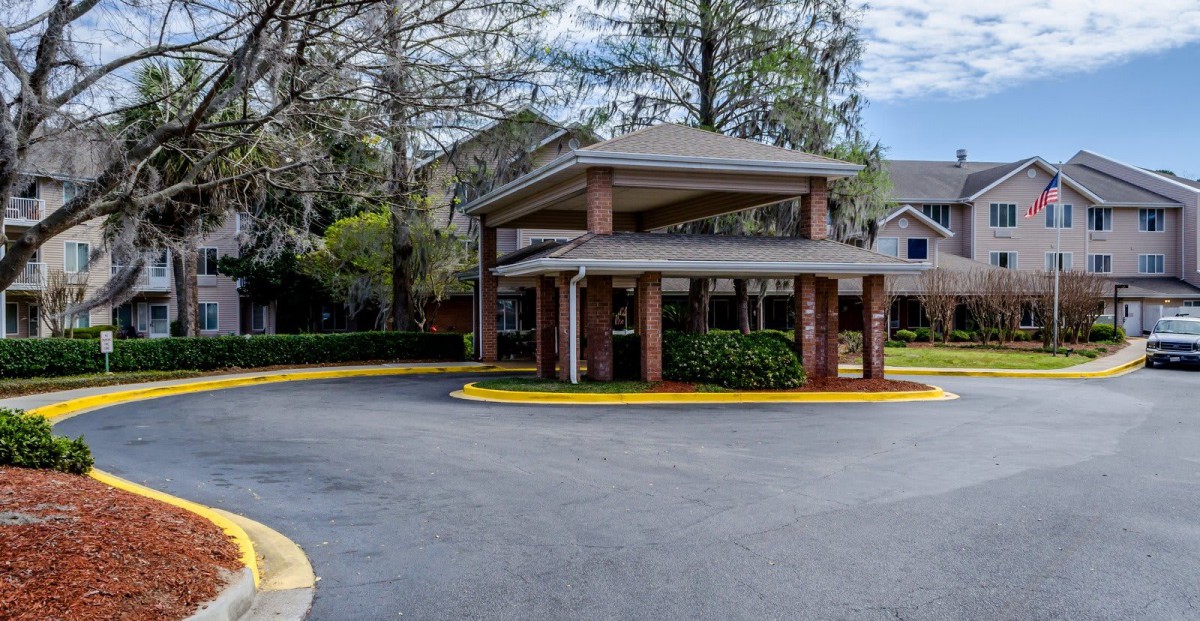 A parking area entrance surrounded by trees, featuring a covered driveway.